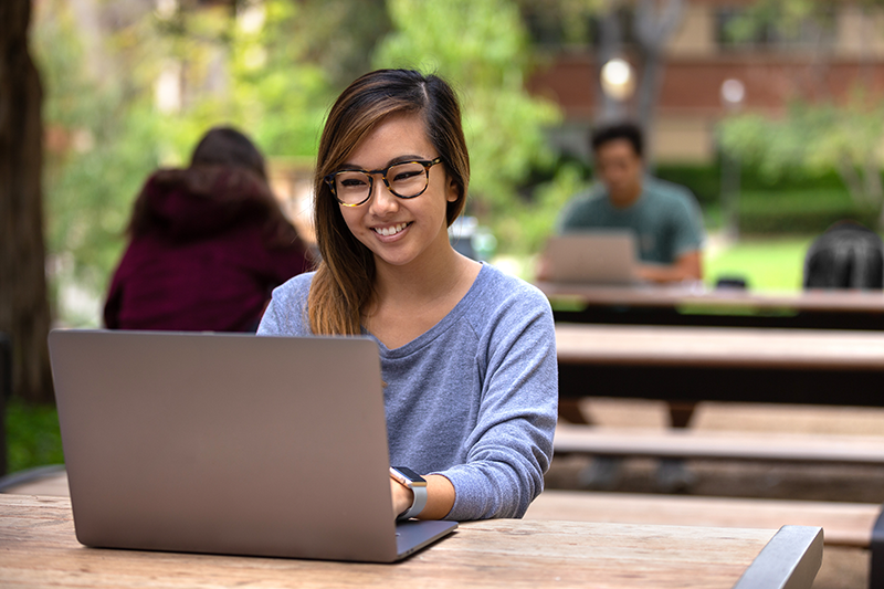 Person at outdoor table studying on laptop